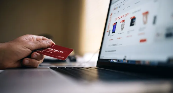 O persoană care are un card în mână, în fața unui laptop.