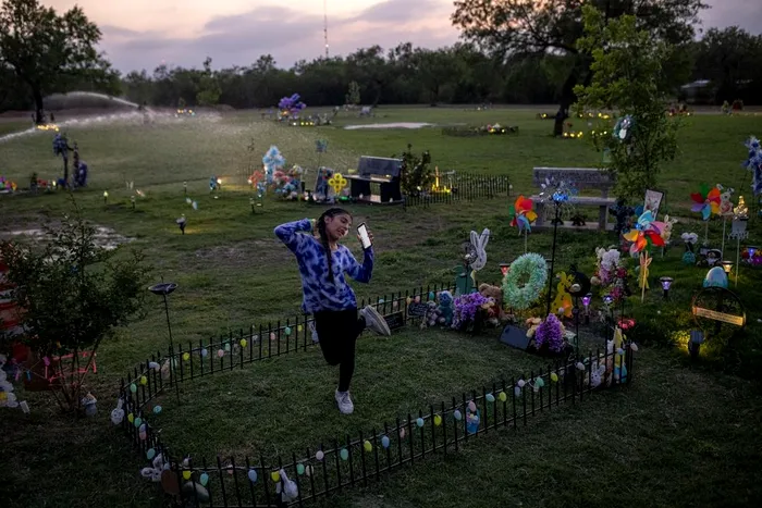 Caitlyne Gonzales, care și-a pierdut mulți dintre prietenii în împușcătură, a cântat și a dansat pe piesele lui Taylor Swift la mormântul lui Jacklyn Cazares din Uvalde, Texas, pe 19 aprilie. La un an după ce 19 copii și doi profesori au fost uciși la școala elementară Robb, cimitirul unde sunt înmormântați cei mai mulți dintre victime a devenit un punct de ancorare în viața familiilor lor. [Sursa imaginii: Tamir Kalifa—The New York Times/Redux]