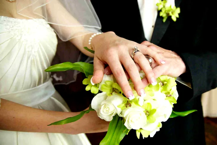 Mâinile mirilor pe buchetul miresei.