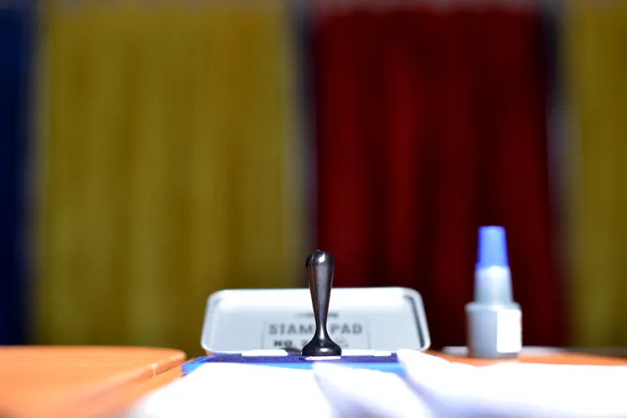 O ștampilă, i tușieră, și pe fundal steagul României.